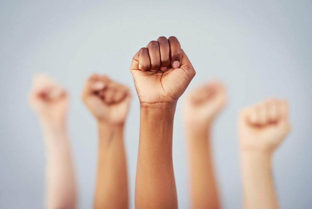 Cropped studio shot of a group of women raising their fists in solidarity against a gray background