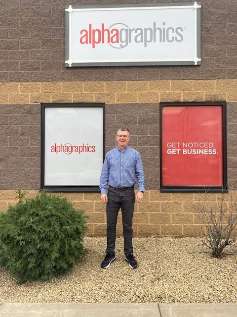 man standing in front of AlphaGraphics storefront